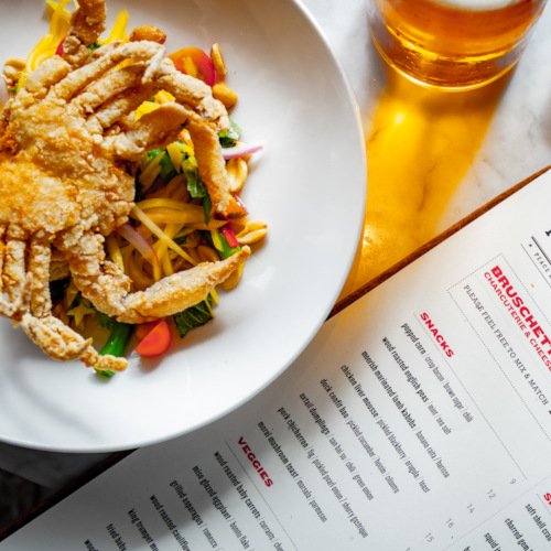 Crab dish with vegetables, a glass of draft beer and menu