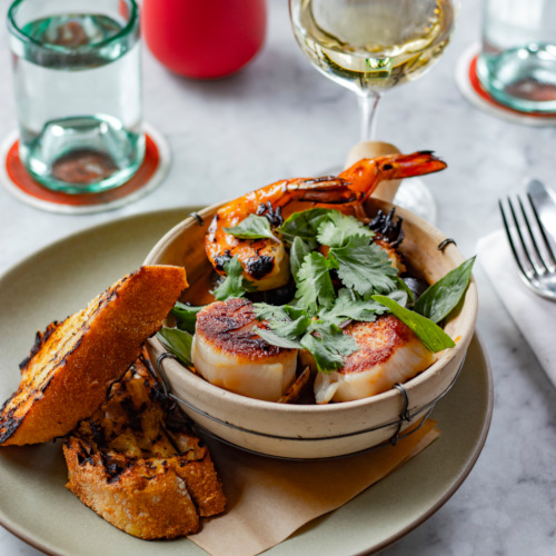 Shrimp and seafood bowl with greens, toast and a glass of white wine